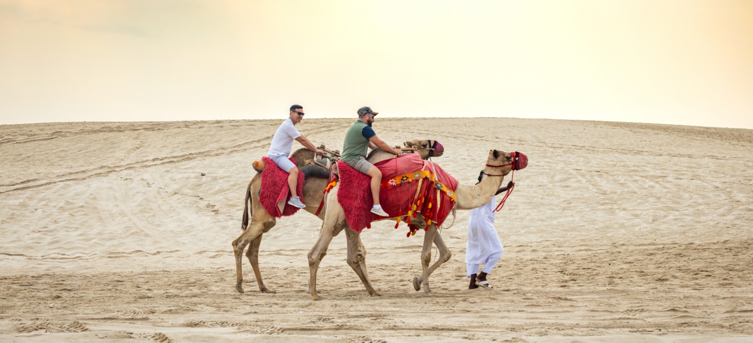 tourists riding camels sealine dunes qatar